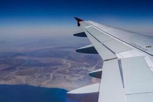 Visão para uma asa a partir de a avião durante uma voar sobre a deserto com a vermelho mar foto