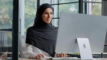 confiante bem sucedido elegante árabe empresária digitando em computador atraente muçulmano fêmea dentro hijab profissional trabalhador com experiência Gerente empreendedor trabalhando dentro moderno escritório posando dentro local de trabalho foto