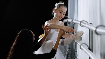 principiante bailarina dentro tutu Adolescência menina escuta para adendo do adulto mulher treinador para aprender para dança juntos dentro dançando escola perto barra. fêmea professor compartilhar experiência ajuda com alongamento postura foto