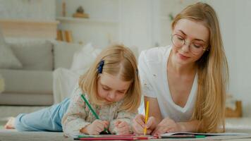 caucasiano mãe deitado do chão às casa com pequeno pequeno adotado criança menina apreciar desenhar junto. filha bebê pré escola criança com mãe babá desenhando cenário com lápis falando feliz família foto