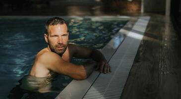 bonito jovem homem relaxante em a Beira do interior natação piscina foto