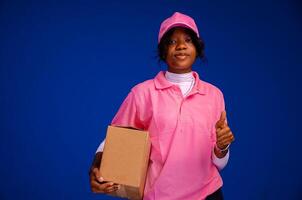 lindo africano fêmea correio trabalhador segurando uma caixa, faz uma polegares acima gesto foto