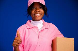 lindo Preto fêmea correio trabalhador segurando uma caixa, faz uma polegares acima gesto foto