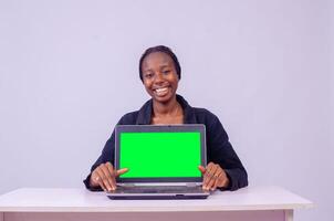 retrato do uma lindo jovem Preto mulher mostrando dela computador portátil tela, ela é sorridente foto
