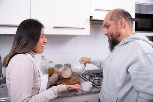 casal fala e tem Diversão enquanto preparando biscoitos às lar. foto