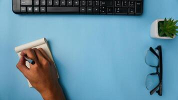 área de trabalho escrivaninha com cadernos, teclado, canetas, copos, plantas em azul fundo foto