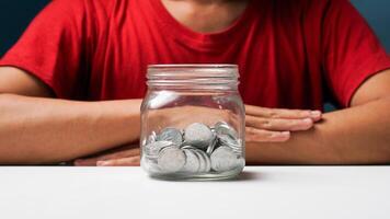 homem com moedas dentro uma Claro transparente vidro jar. salvando dinheiro conceito foto