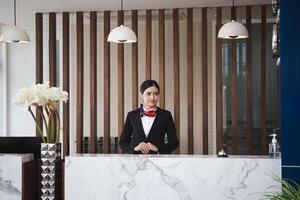 jovem mulher recepcionista em pé às a hotel recepção contador, retrato do fêmea recepcionista trabalhando dentro Hostel foto