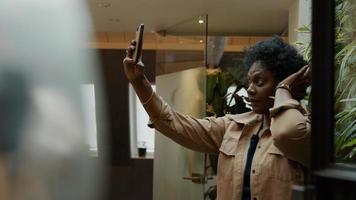 mulher madura negra segurando o celular no ar, ajeitando o cabelo, olhando para o telefone foto