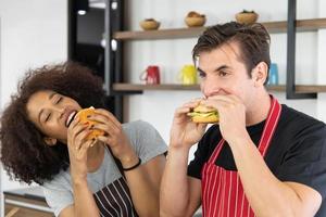 jovem casal está se alimentando enquanto cozinha hambúrguer na cozinha foto