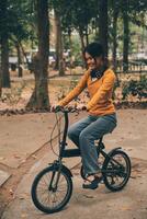 feliz jovem ásia mulher enquanto equitação uma bicicleta dentro uma cidade parque. ela sorriu usando a bicicleta do transporte. ambientalmente amigáveis conceito. foto