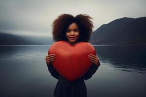 ai gerado africano americano mulher segurando grande vermelho coração dentro frente do escandinavo estilo lago às nebuloso nublado dia, neural rede gerado fotorrealista imagem foto