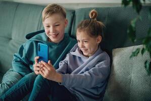 dois crianças sentado em uma sofá olhando às uma telefone foto
