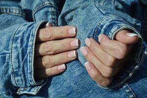 delicado manicure com camuflar gel polonês para quadrado unhas com uma francês Projeto. mãos com profissional manicure em a fundo do uma jeans jaqueta. foto