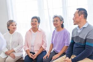 Senior fêmeas e masculino sentado em banco. Mais velho pessoas estão ouvindo e apreciar encontro foco grupo às vivo sala. alegre despreocupado aposentado Senior amigos desfrutando relaxamento às aproximadamente lar. foto