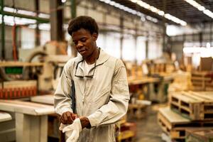 africano homem trabalhadores Engenharia em pé com confiança com trabalhando suíte vestir e mão luva dentro frente máquina. conceito do inteligente indústria trabalhador operativo. madeira fábrica produzir madeira palato. foto