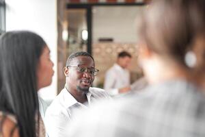 foco do inteligente africano homem de negocios. diverso empregados colhido dentro escritório tendo Diversão debate enquanto discutindo Novo Ideias projeto. multirracial colegas de trabalho encontro às coworking espaço área. foto