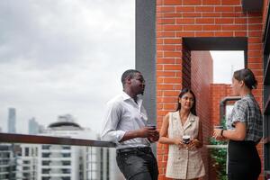 equipe do o negócio pessoas inteligente homem e mulheres ficar de pé às ao ar livre terraço construção e conversa juntos com café da manhã Comida e café em a mão dentro Boa sentindo-me com cidade espaço prédio. o negócio manhã. foto