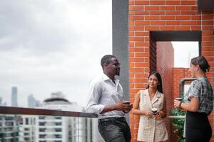 equipe do o negócio pessoas inteligente homem e mulheres ficar de pé às ao ar livre terraço construção e conversa juntos com café da manhã Comida e café em a mão dentro Boa sentindo-me com cidade espaço prédio. o negócio manhã. foto