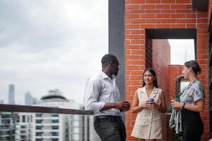 equipe do o negócio pessoas inteligente homem e mulheres ficar de pé às ao ar livre terraço construção e conversa juntos com café da manhã Comida e café em a mão dentro Boa sentindo-me com cidade espaço prédio. o negócio manhã. foto