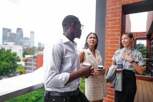 equipe do o negócio pessoas inteligente homem e mulheres ficar de pé às ao ar livre terraço construção e conversa juntos com café da manhã Comida e café em a mão dentro Boa sentindo-me com cidade espaço prédio. o negócio manhã. foto