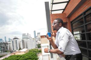 africano o negócio inteligente homem carrinhos às ao ar livre terraço prédio. pessoas com em mão dentro Boa sentindo-me com cidade espaço prédio. relaxante do pessoas o negócio manhã. foto