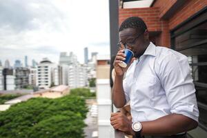 africano o negócio inteligente homem carrinhos às ao ar livre terraço prédio. pessoas com em mão dentro Boa sentindo-me com cidade espaço prédio. relaxante do pessoas o negócio manhã. foto