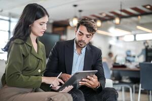 o negócio pessoas falando às local de trabalho escritório. masculino e fêmea colegas apreciar relaxante e sentado em sofá. colegas discutindo sobre a projeto dentro a escritório. equipe do jovem pessoas dentro escritório. foto