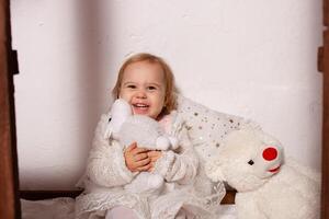 uma pequeno menina com brinquedos dentro uma de madeira casa. foto estúdio com Natal decorações. uma feliz criança tocam com brinquedos