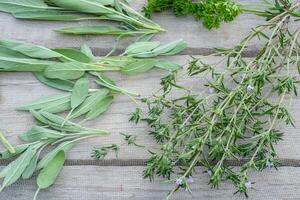 secagem fresco ervas e vegetação para especiaria Comida em de madeira escrivaninha fundo. salsinha folhas, sábio e Manjerona. foto