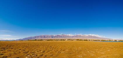 campo coberto com seco Relva solavancos com pequeno quirguiz Cidade balykchi e Alto montanhas em a horizonte, Largo ângulo panorâmico Visão foto