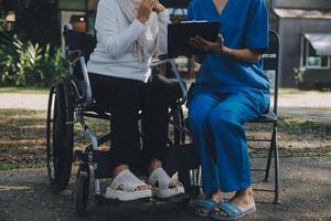 uma enfermeira levar Cuidado uma Senior masculino em cadeira de rodas dentro dele jardim às casa foto