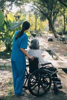 uma enfermeira levar Cuidado uma Senior masculino em cadeira de rodas dentro dele jardim às casa foto