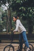 feliz ásia jovem mulher andar e passeio bicicleta dentro parque, rua cidade dela sorridente usando bicicleta do transporte, eco amigável, pessoas estilo de vida conceito. foto