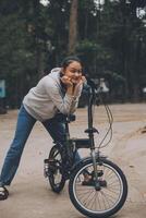 feliz ásia jovem mulher andar e passeio bicicleta dentro parque, rua cidade dela sorridente usando bicicleta do transporte, eco amigável, pessoas estilo de vida conceito. foto