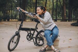 feliz ásia jovem mulher andar e passeio bicicleta dentro parque, rua cidade dela sorridente usando bicicleta do transporte, eco amigável, pessoas estilo de vida conceito. foto