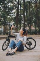 feliz ásia jovem mulher andar e passeio bicicleta dentro parque, rua cidade dela sorridente usando bicicleta do transporte, eco amigável, pessoas estilo de vida conceito. foto