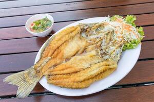 frito pargo peixe em branco dentro branco prato em madeira mesa servido com peixe molho e legumes. foto