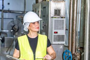 fêmea industrial engenheiro vestindo uma branco capacete enquanto em pé dentro uma pesado industrial fábrica foto