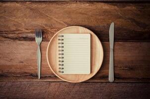 caderno dentro a de madeira prato com uma colher e uma faca deitado ao lado uma mesa, conceito para percepção foto