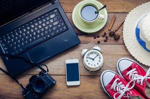 café xícara, caderno, alarme relógio fone de ouvido inteligente telefone e traje em a de madeira chão dentro a manhã. foto