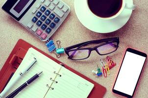 uma copo café inteligente telefone e escritório suprimentos em a mesa foto