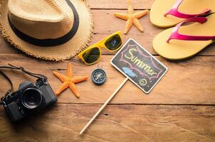 mar viagem acessórios uma chapéu, oculos de sol, Câmera. colocada em de madeira com palavra verão em quadro-negro foto