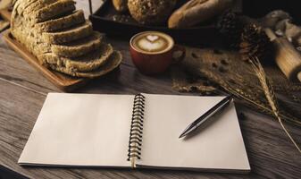 a caneta é colocada em uma branco caderno espalhar em uma mesa com café e pão colocada. foto
