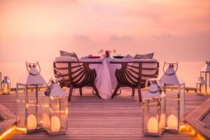 incrível jantar romântico na praia no deck de madeira com velas sob o céu pôr do sol. romance e amor, jantar de destino de luxo, configuração de mesa exótica com vista para o mar foto