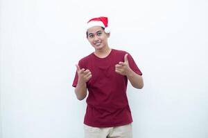 jovem ásia homem vestindo uma santa claus chapéu sorridente, choque e apontando para dela lado isolado de branco fundo para visual comunicação foto