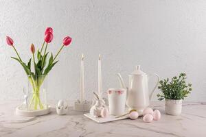 lindo festivo composição para Páscoa feriado em mármore bancada do luz cozinha. velas, uma vaso do tulipas, Páscoa ovos e coelhinhos. foto