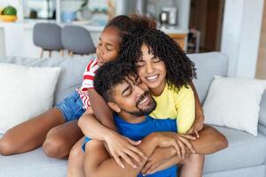 feliz alegre família pai, mãe e filha tendo Diversão abraço em sofá às casa. foto