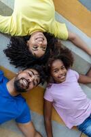 família fim de semana. sorridente Preto mãe, pai e filha deitado em cama junto, relaxante às lar. foto