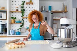 cozimento conceito. retrato do alegre mulher amassar massa dentro cozinha interior, alegre fêmea dentro avental tendo Diversão enquanto preparando caseiro pastelaria, foto